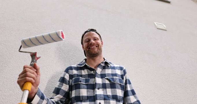 Smiling man holding paint roller ready for house painting and renovation. handyman service
