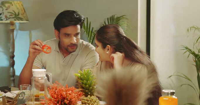 Indian happy man woman couple sitting around table chair talk speak share gossip room place young adult gen z male hold roti bowl serve fresh salad female eat tasty food spend time enjoy dinner night