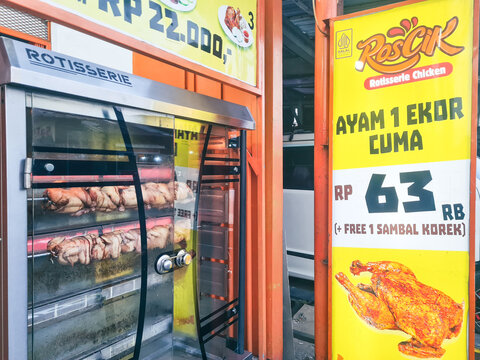 Depok, Indonesia - August 2, 2026: Roscik rotisserie chicken stall showing whole chickens roasting in a machine with pricing signage in West Java.