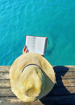 woman with big hat reading a book at the lake