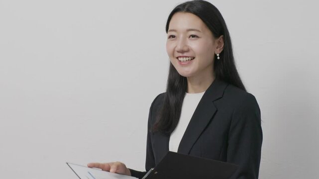 Young Japanese businesswoman holding file smiling in front of white wall