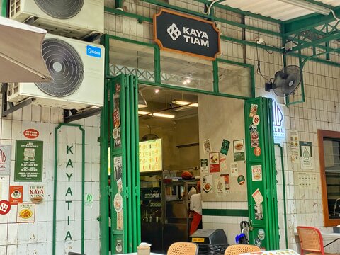 Jakarta, Indonesia - July 17, 2026: The retro-styled storefront and entrance of a local kopitiam cafe named Kaya Tiam, featuring green folding doors and vintage promotional posters in the Blok M area.