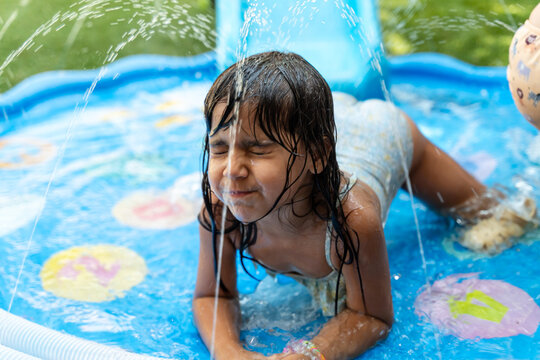 A young white girl plays and splashes in an inflatable paddling pool