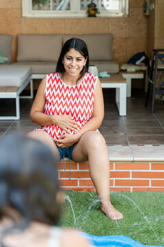 Pregnant white woman sitting outdoors holding her belly in a backyard