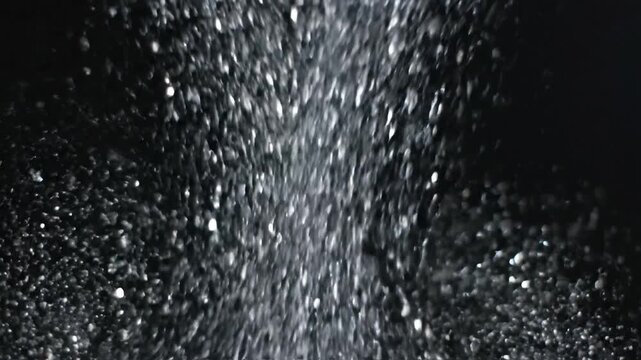 Shimmering silver glitter particles falling against a dark background for festive luxury design
