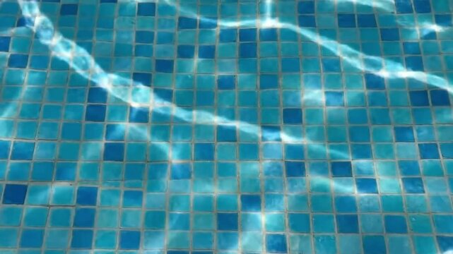 Shimmering sunlight creates abstract caustic patterns on the blue mosaic tiles of a swimming pool