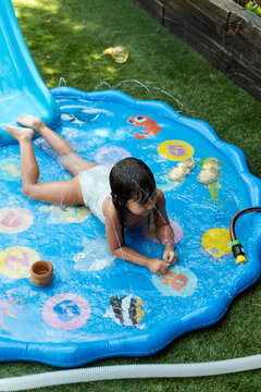 White Child playing on inflatable splash pad with water sprays
