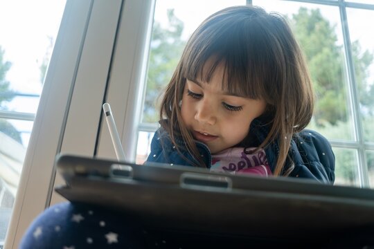 Young white girl using a digital tablet indoors near a window