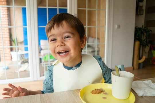 A toddler happily eating a snack indoors featuring a white model