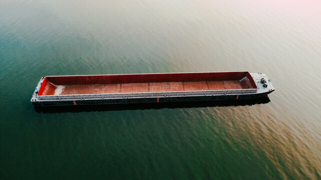 An empty river transport barge on the Danube River during a sunset. Aerial view of an empty river transport barge. Transport barge