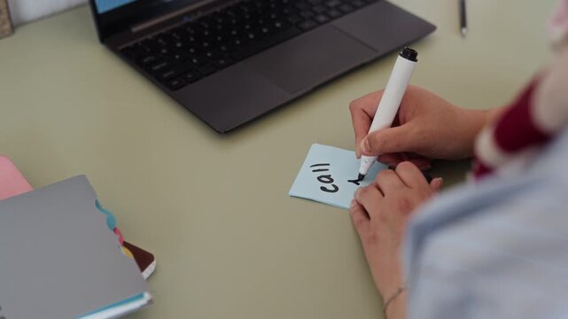 Young Muslim woman writing reminder on sticky note and pinning it to corkboard in office. Footage is ideal for corporate productivity, time management, and task planning concepts