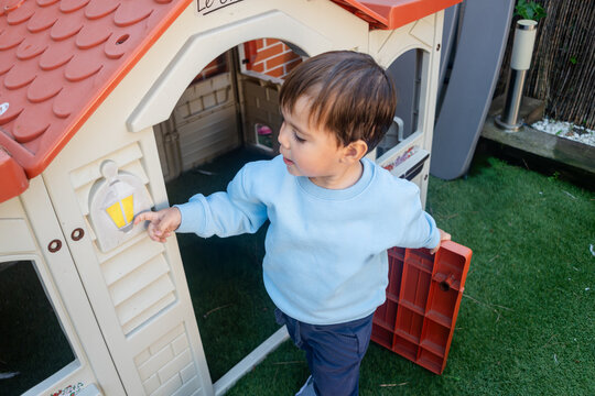 A toddler white boy plays with a plastic playhouse outside in Madrid