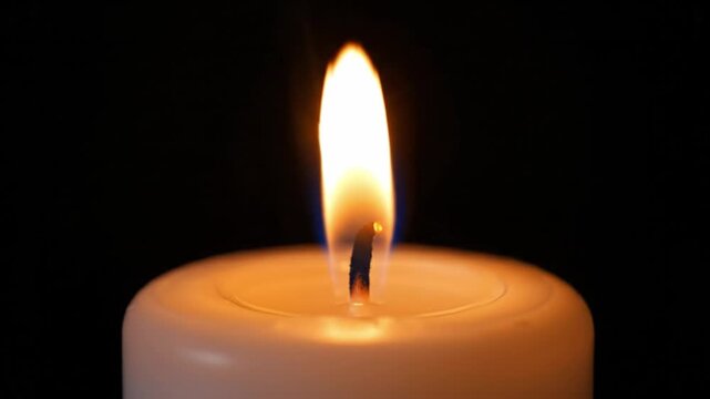 Single white candle burning with a flickering flame against a dark black background