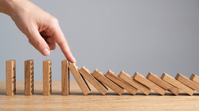 Finger touching wooden domino, starting a chain reaction, symbolizing consequence, cause and effect, and risk management