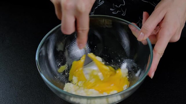 Close-up of hands mixing egg yolks with fork in glass bowl during cooking, set in Cooking location, daytime kitchen scene.