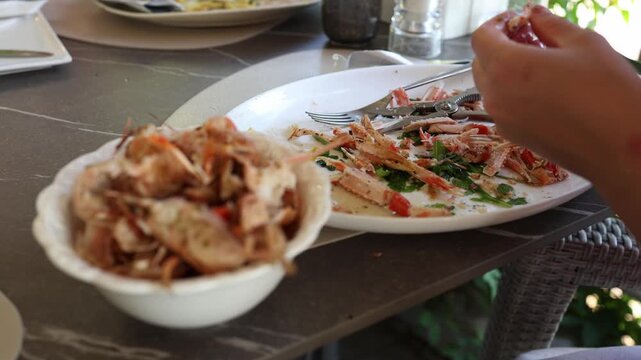 Hands peel grilled langoustines at a restaurant table with empty shells and seafood leftovers showing a casual dining moment during a sunny summer vacation by the seaside