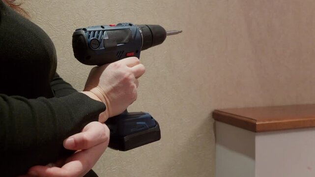 Worker grips cordless power drill with rotating bit extended, demonstrating tool operation indoors. Includes original audio of device sound effects.