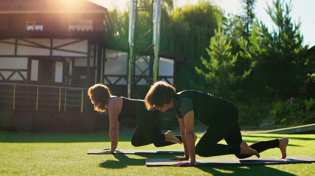 Elderly women practicing slow motion Pilates outdoors on yoga mats, performing graceful balance poses together on a sunny day to enhance strength, flexibility, and wellbeing