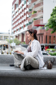 Side View of Asian Woman Typing on Laptop Computer Outdoors