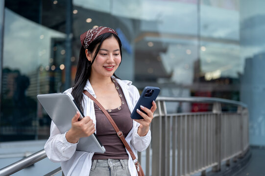 Asian Woman Looking at Smartphone while Carrying Laptop