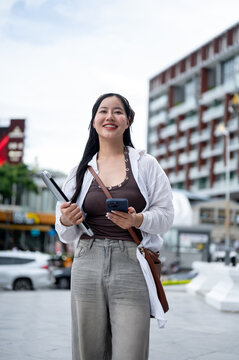 Low Angle Shot of Asian Woman Standing Outdoors with Laptop and Phone