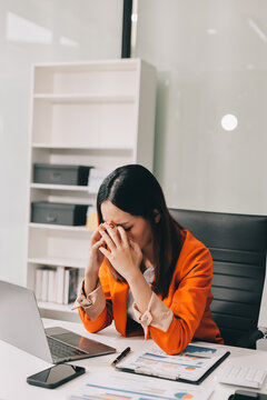 Office Discomfort: A female office worker in a red shirt experiences neck pain while working on her laptop, surrounded by office supplies and a calculator, indicating a stressful work environment.