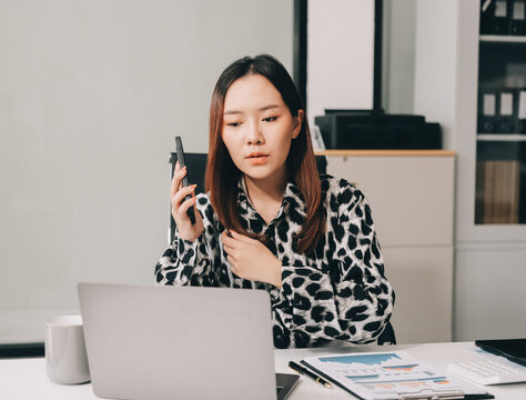 Office Discomfort: A female office worker in a red shirt experiences neck pain while working on her laptop, surrounded by office supplies and a calculator, indicating a stressful work environment.