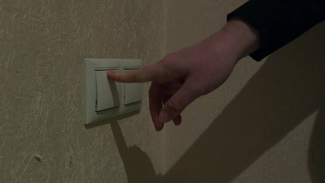 Person flips light switch off on beige wall with textured surface, capturing real switching action with original sound.