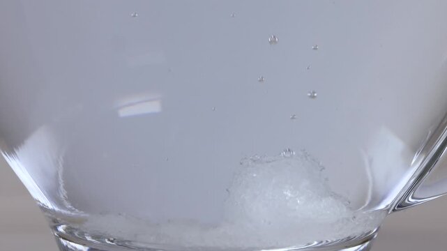 White Sugar Crystals Dissolving in a Clear Glass Mug of Water
