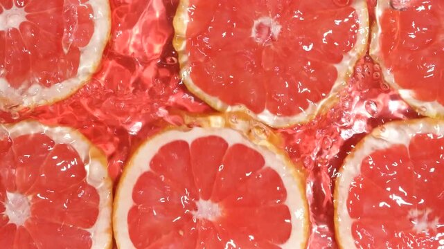 Slow motion of fresh grapefruit slices under rippling water with bubbles.