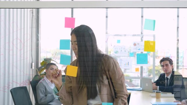 Female professional presenting ideas on glass board, business meeting, project discussion, office teamwork, corporate communication, planning session, workplace collaboration.