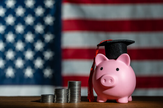 US college education savings and student loan concept. Pink piggy bank wearing graduation cap and coin stacks, against USA flag backdrop, representing American tuition costs and financial planning