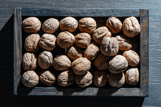 Whole walnuts in wooden box. Top view of raw whole walnuts in shells neatly arranged in rustic dark wooden tray crate on table, dramatic side lighting for organic health food marketing concept