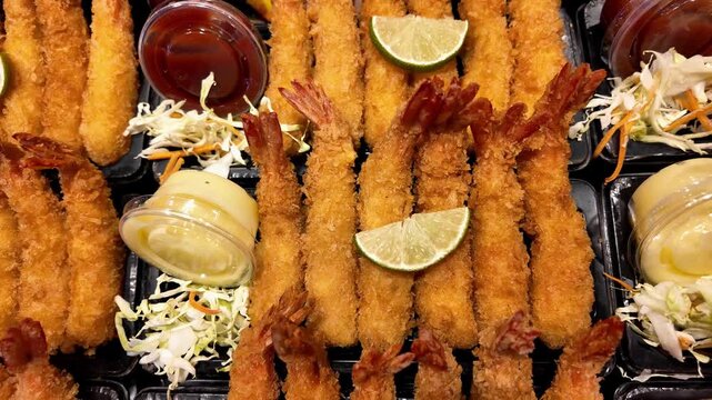 Close-up of crispy breaded shrimp platters served with lemon wedges, fresh salad and dipping sauces at a Thai street food market. Golden fried seafood ready to eat, beautifully presented for takeaway.