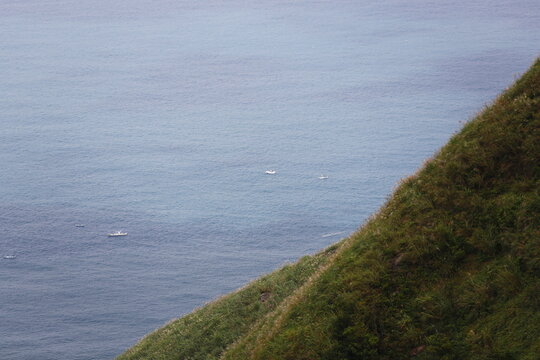 Fishing Boats Drift Below a Steep Coastal Hillside.