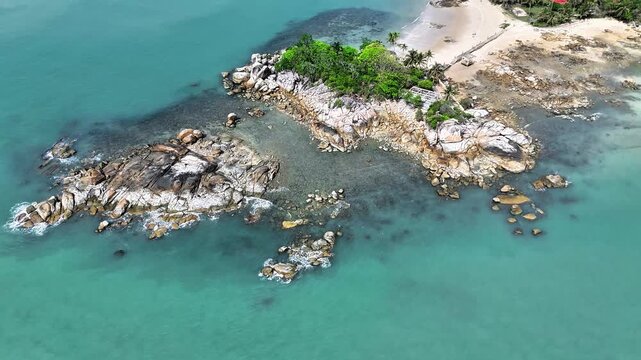 Beautiful tropical granite coast surrounded by clear turquoise ocean, gentle waves, scenic rocky peninsula and peaceful beach aerial view