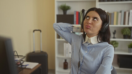Obraz premium Woman wearing headset and microphone speaks at desk while touching headphones and pointing to computer screen in building; concentration.