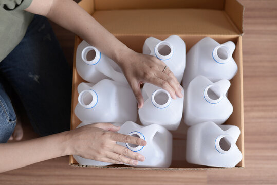 Woman packing empty white plastic gallon containers into cardboard box for recycling, top view