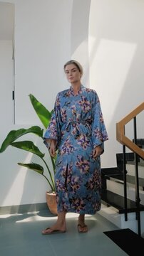 Elegant woman wearing luxury kimono robe in modern tropical home.