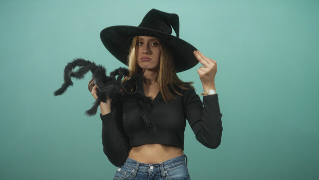 Woman holds a large black spider and makes a two finger spell gesture in studio; mischievous halloween fun.