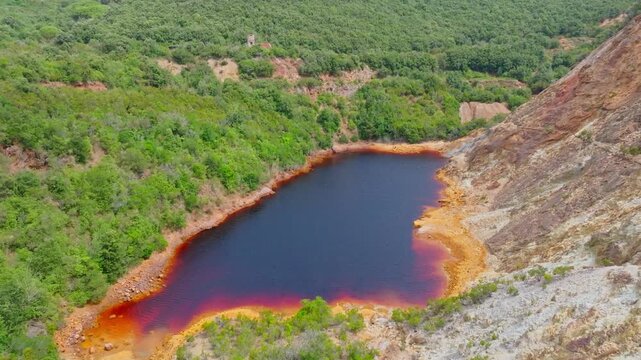Aerial view of the red-hued Laghetto delle conche surrounded by lush green vegetation and rocky terrain in the old mining area of Rio Marina, Toscana, Italy