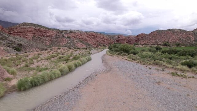 4K drone aerial view of La Poma, Salta, Argentina. Stunning Andean landscape with red rock mountains, green valleys and a river crossing the dramatic canyon scenery.