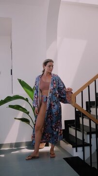 Elegant woman wearing luxury kimono robe over  swimsuit in modern tropical villa.
