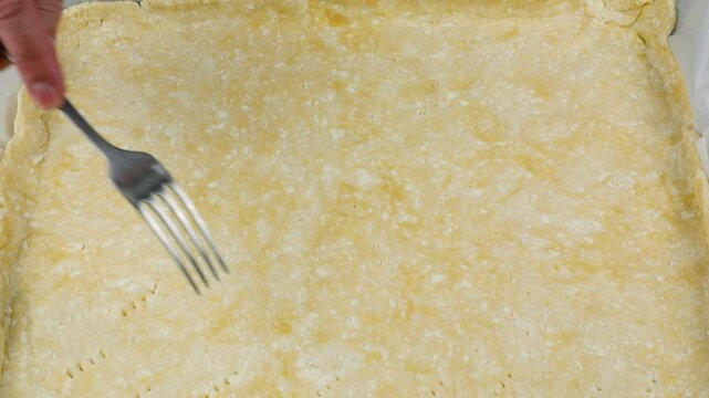 A close-up of professional hands using a fork to prick small holes in a raw cottage cheese dough base on parchment paper to let steam escape and prevent uneven rising.