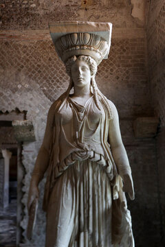 Statua monumentale di Cariatide in marmo a Villa Adriana raffigurante una figura femminile classica con capitello sulla testa all'interno di rovine antiche a Tivoli