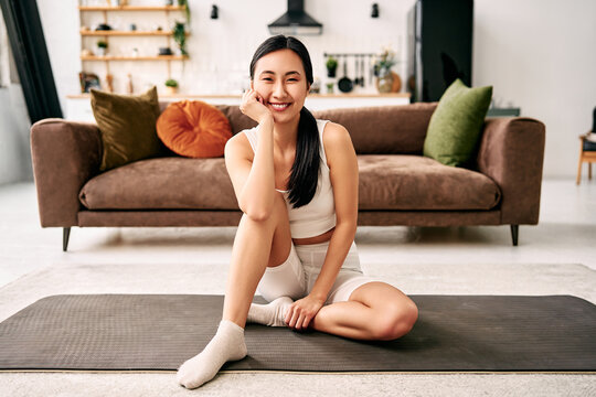 Smiling woman relaxing on yoga mat at home.