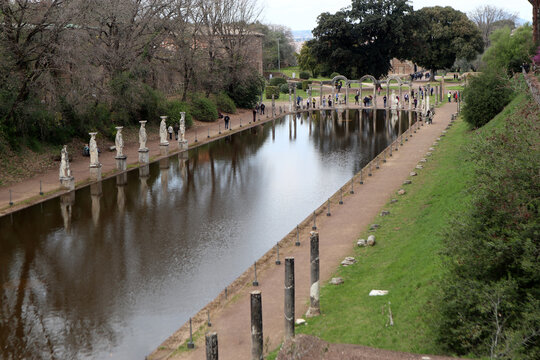Grande vasca d'acqua del Canopo a Villa Adriana con statue classiche, cariatidi e turisti riflessi sulla superficie, Tivoli, Italia