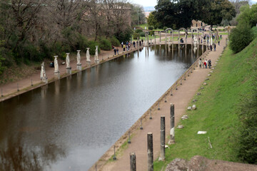 Fototapeta premium Grande vasca d'acqua del Canopo a Villa Adriana con statue classiche, cariatidi e turisti riflessi sulla superficie, Tivoli, Italia