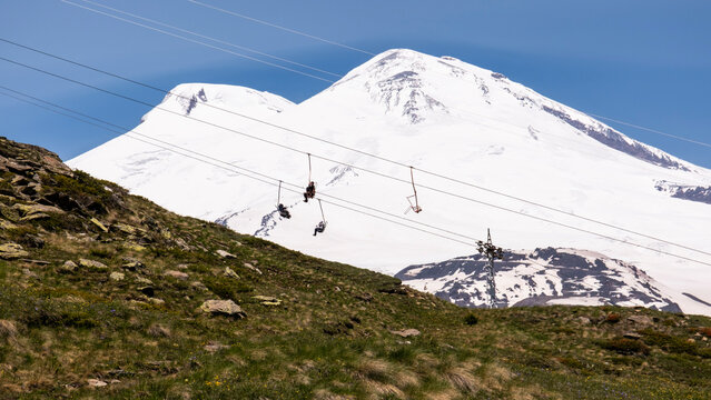 People sitting on a chairlift with Mount Elbrus in the background, Russia