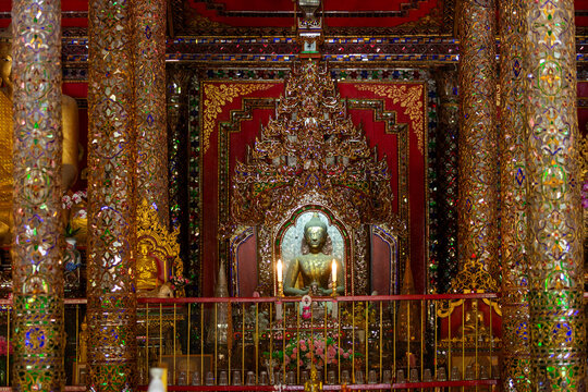 Ornate interior of a Thai temple featuring a golden Buddha statue framed by mosaic columns.